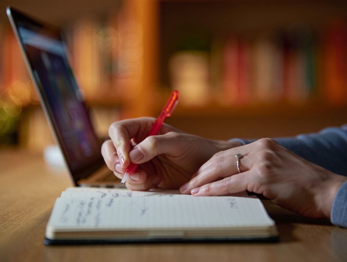 Психолог сидит за ноутбуком и записывает что-то в тетрадь